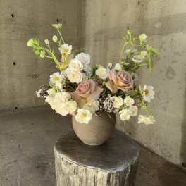Blush and white roses with small white daisies in a beige vase