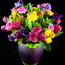 Colorful bouquet of tulips, roses, and carnations in a purple vase