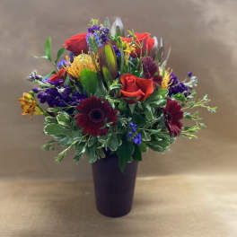 Mixed bouquet of red roses, burgundy daisies, and purple flowers in a dark vase