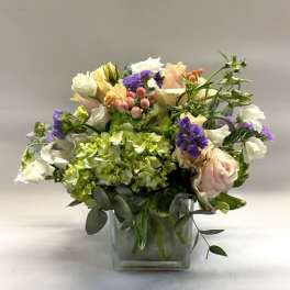 Mixed bouquet in a clear square vase with pink, white, purple, and green blooms