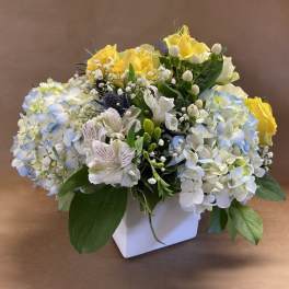 Bouquet of yellow roses and pale blue hydrangeas in a white vase