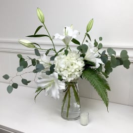 White lilies and hydrangea in a clear glass vase with eucalyptus