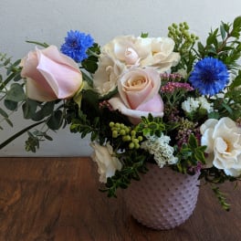 Mixed bouquet of pale roses, white blooms, and blue flowers in a textured vase