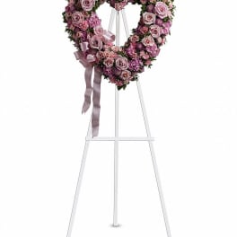 Heart-shaped pink floral wreath on a white easel with ribbon