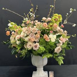Large floral arrangement in a white pedestal vase with pink roses and green orchids