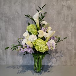 Tall bouquet of white calla lilies, hydrangeas, and lavender flowers in a glass vase