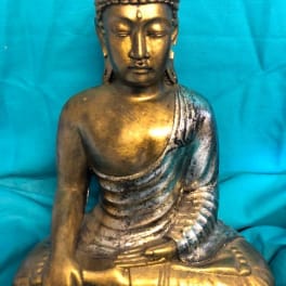 Gold Buddha statue seated against a blue fabric background