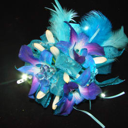 Blue and purple floral corsage with feathers and ribbon on a black background