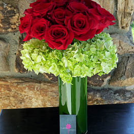 Red roses above a green hydrangea cluster in a tall glass vase