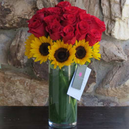 Red roses and yellow sunflowers in a tall glass vase