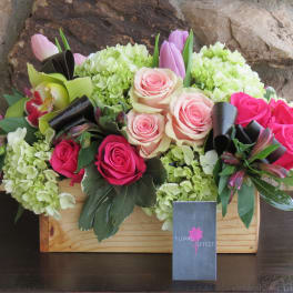 Mixed pink and cream roses in a wooden box with green hydrangeas.