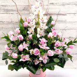 Pink roses and white orchids in a pink hatbox arrangement