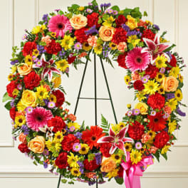 Large colorful floral wreath on a black stand with a pink ribbon