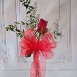 Single red rose in a clear vase with a large red bow