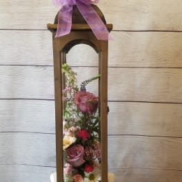 Tall wooden lantern with a pink ribbon and mixed flowers inside