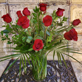 Red roses arranged in a clear glass vase with greenery