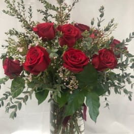 Red roses arranged in a clear glass vase with airy greenery