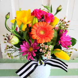 Bright mixed bouquet in a white vase with a black-and-white ribbon