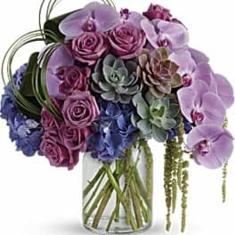 Bouquet of purple orchids, pink roses, and succulents in a glass vase