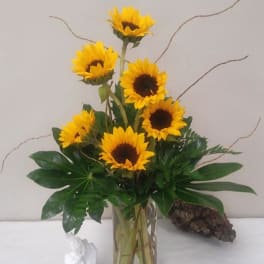 Sunflower arrangement in a clear glass vase with decorative figurines