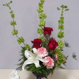Arrangement of red roses, white lily, and pink flowers in a black vase