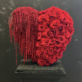 Heart-shaped red rose arrangement with cascading red strands on a black pedestal