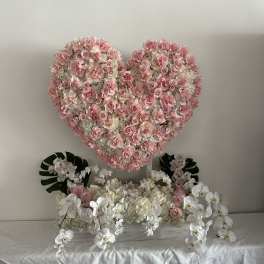 Heart-shaped pink rose arrangement above white orchids and pale flowers