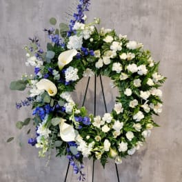 Large floral wreath with white calla lilies and blue flowers on a stand