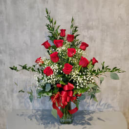 Red roses arranged in a clear glass vase with baby's breath and greenery