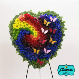 Heart-shaped floral arrangement in rainbow colors with butterfly accents on a stand