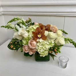 Mixed bouquet with white roses, pale hydrangeas, and orange orchids in a green vase