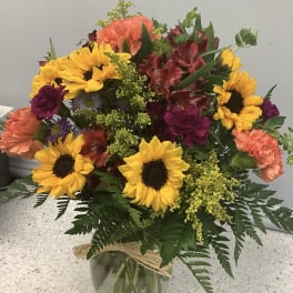 Mixed bouquet with sunflowers, carnations, and alstroemeria in a glass vase
