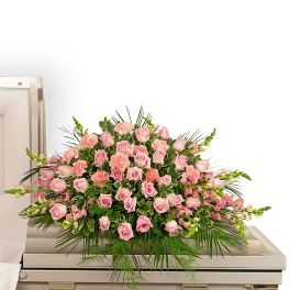 Large pink rose and carnation casket spray displayed on a light-colored casket
