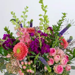Mixed bouquet of pink and purple flowers with green spikes in a clear glass vase