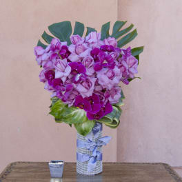 Pink roses and purple orchids arranged in a silver vase with a blue ribbon