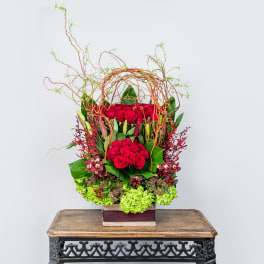 Tall arrangement of red roses with green accents in a square container