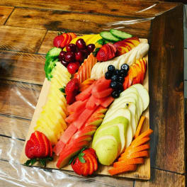 Fruit platter with sliced strawberries, melon, grapes, pears, and oranges on a wooden board