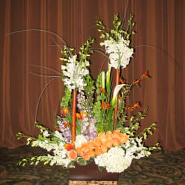 Tall floral arrangement with orange roses and white orchids in a basket vase