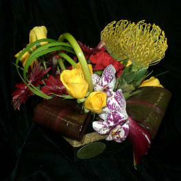 Mixed bouquet with yellow roses, orchids, and red flowers in a low container