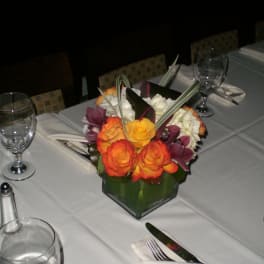 Table centerpiece with orange and purple flowers in a green glass vase