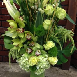 Tall green floral arrangement with orchids, roses, lilies, and hydrangeas in a rectangular vase