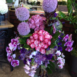 Tall floral arrangement with pink roses, purple allium, and orchids