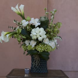 White calla lilies and roses arranged in a dark textured vase