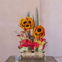 Tall floral arrangement with sunflowers, roses, and calla lilies in a wooden stand
