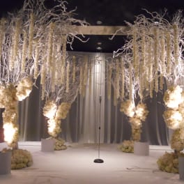 Tall white floral installations frame a stage with a microphone stand
