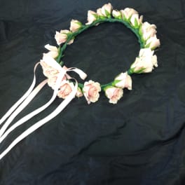 Pink rose flower crown with white ribbon ties on a dark fabric background