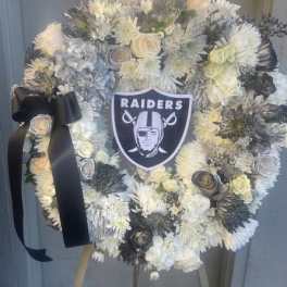 White floral wreath with a Raiders emblem and black ribbon on an easel