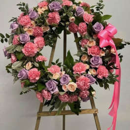 Standing wreath of pink carnations and lavender roses with a pink bow on a wooden easel