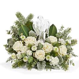 White roses and greenery arranged around a clear angel figurine
