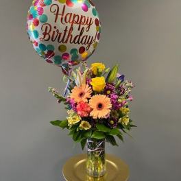 Birthday balloon above a mixed flower bouquet in a glass vase